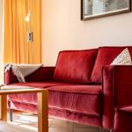Roter Samtsofa mit Kissen und Decke vor Fenster mit orangefarbenen Vorhängen.
