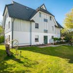 Haus mit weißer Fassade, grüner Tür und gepflegtem Garten unter blauem Himmel.