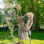 Garten mit Baumstumpf, Körben und Gartenlampen. Gras und Sträucher im Hintergrund.