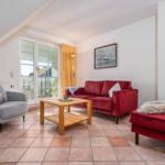 Wohnzimmer mit rotem Sofa, grauer Sessel und Terrasse. Holztisch und Wandbild.