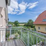 Terrasse mit Blick auf grüne Landschaft und benachbarte Häuser unter blauem Himmel.
