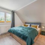 Schlafzimmer mit Dachschrägen, Bett mit grünem Überwurf und Fenster mit Blick auf Bäume.