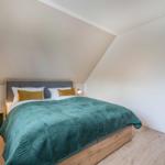 Schlafzimmer mit Dachschrägen, Bett mit grünem Daunendeckel und zwei Nachttischen.