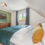 Schlafzimmer mit Doppelbett, Fenster und Fernseher an der Wand.