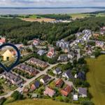 Luftbild eines Dorfes mit Häusern, Wäldern und einem großen See im Hintergrund.