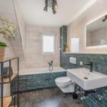 Bad mit Badewanne, Waschbecken und Toilette. Wandverkleidung in dunkelblau und hellbeige Fliesen.