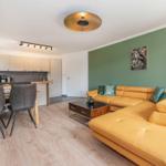 Wohnzimmer mit gelbem Sofa, grüner Wand und Essbereich mit Holzboden.