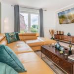 Ein Wohnzimmer mit braunem Sofa, Holztisch und Fernseher an der Wand.