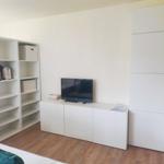 Zimmer mit weißen Schränken, Fernseher und Küchenutensilien auf Regalen.