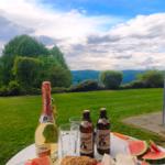 Tisch mit Wassermelone, Bier und Champagner im Garten mit Blick auf grüne Landschaft.