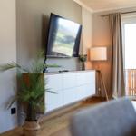 Wohnzimmer mit Fernseher, Sideboard, Pflanze und Balkonansicht.