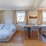Wohn- und Essbereich mit Sofa, Tisch und Stühlen. Fenster mit Blick auf Berge.
