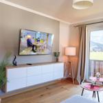Wohnzimmer mit TV, Balkon und Bergblick. Holzboden, Couch und dekorative Pflanzen.