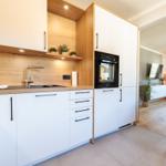 Moderne Küche mit Holzoptik und integriertem Backofen. Wohnbereich mit TV und Blick auf Landschaft.
