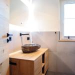 Badezimmer mit Steinwaschbecken auf Holzunterschrank und Fenster mit Pflanze.