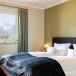 Schlafzimmer mit Blick auf Berge. Bett mit weißen Kissen und dunkler Decke.