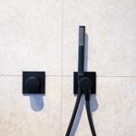 Duschkopf und Drehregler an Wand mit Mosaikfliesen