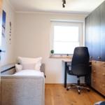 Schlafzimmer mit Bett, Schreibtisch und Schrank. Holzboden und Fenster mit Pflanzen.