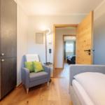 Schlafzimmer mit Bett, Sessel und Kleiderschrank. Tür führt in Schlafbereich mit Blick.