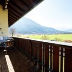Terrasse mit Sitzgelegenheit und Blick auf grünes Feld und Berge.