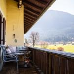 Terrasse mit Sitzgruppe und Blick auf grünes Feld und Berge.