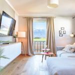 Wohnzimmer mit Sofa, Fernseher und Balkonblick auf Berge.