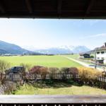Blick von Balkon auf grünes Feld, Straße und Berge mit Schnee.