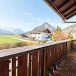 Terrasse mit Holzgeländer und Blick auf grünes Feld und Berge.