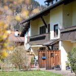 Haus mit Balkonen, Holztür und Garten. Berglandschaft im Hintergrund.