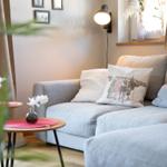 Ein grauer Sofa mit Kissen, zwei runde Tische und eine Wandlampe.