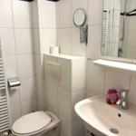Badezimmer mit Toilette, Waschbecken und Dusche. Weiße Fliesen und Spiegel.