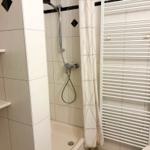 Dusche mit Duschbrause, Handtuchhalter und Wandregal