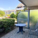 Terrasse mit Tisch und zwei Stühlen, umgeben von Grünflächen und einem Glaswandschutz.