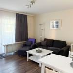 Wohn- und Essbereich mit Sofa, Tisch und Fenster. Holzboden und weiße Möbel.