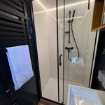 Shower with glass enclosure, handheld shower, and towel warmer.