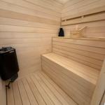 Sauna with wooden bench, basket, and heater on the wall.