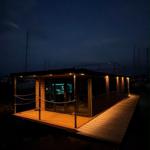 Modern houseboat with wooden deck and lit windows at night.