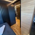 Bedroom with bed, wooden floor, and modern lighting. Door leads to adjacent room.