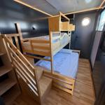 Room with bunk bed and wooden staircase. Wooden floor and dark walls.