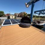 Deck with sun lounger, solar panels, and view of harbor and cranes.