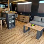 Living kitchen with wooden floor, sofa, dining table, and kitchen island with stools.