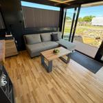 Living area with sofa, table, and wooden floor. Entrance to terrace with garden view.