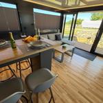 Dining area with wooden floor and seating. Passage to terrace with garden view.