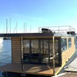 Modern houseboat with wooden cladding and large glass area by the water.
