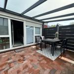 Terrace with seating under glass roof. Red brick paving and black wooden fence.