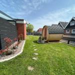 Backyard with sauna, lawn, and plants. Modern facade and fence visible.