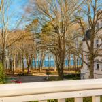 Blick vom Balkon auf Wald und Meer mit weißem Haus im Hintergrund.