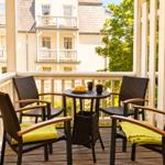 Terrasse mit Tisch und vier Stühlen, grüne Kissen, Blick auf Gebäude und Bäume.