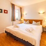 Ein Schlafzimmer mit Doppelbett, Holzboden und Fenster mit Vorhängen.