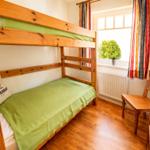 Ein Schlafzimmer mit Doppelstockbett, Holzboden und Fenster mit Vorhängen.
